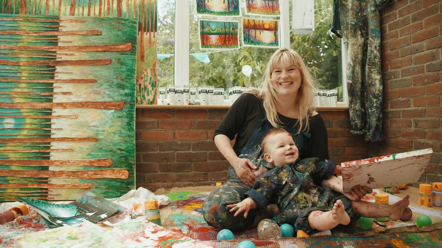 Artist Scarlett Raven painting in her home studio with her toddler son Harvey 3 